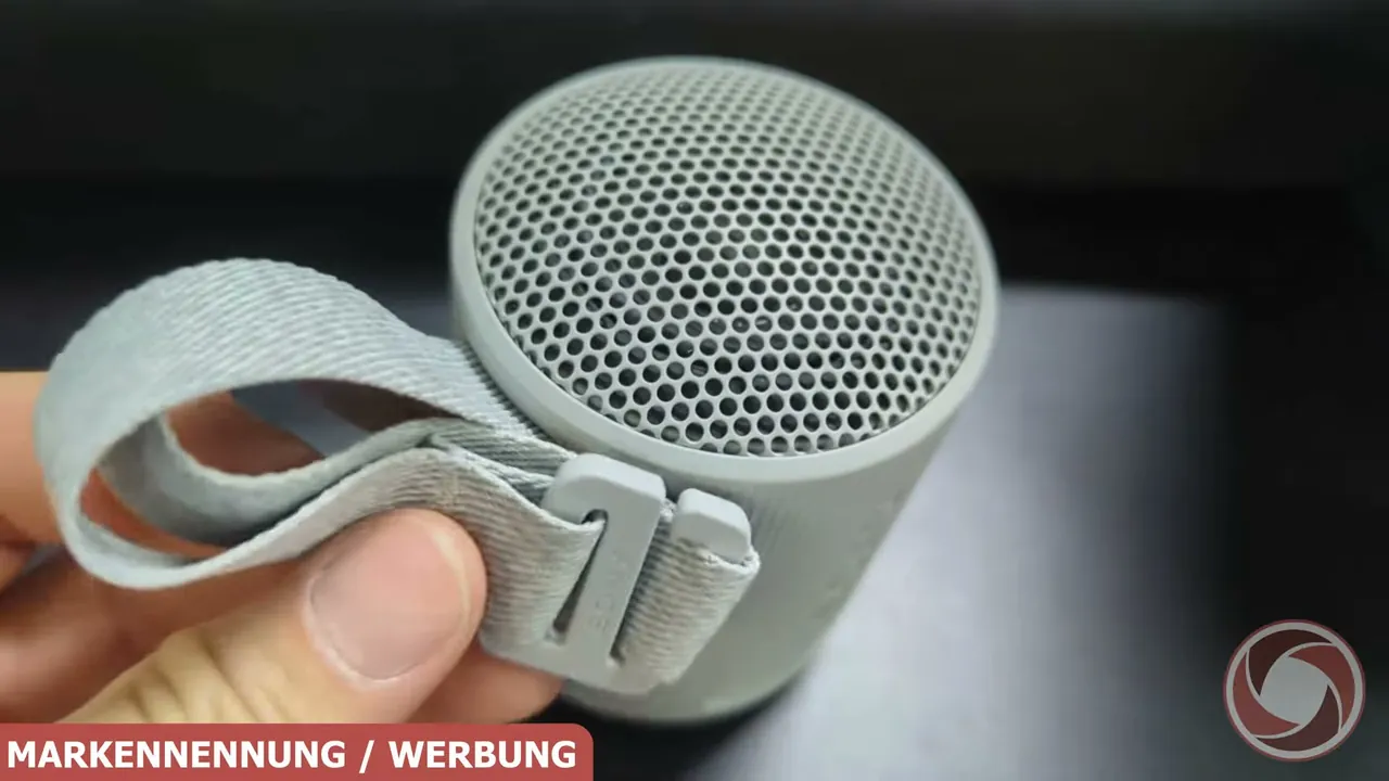 Über das obere Gitter wird der Klang verteilt, während der praktische Trageriemen das Befestigen an Taschen ermöglicht.