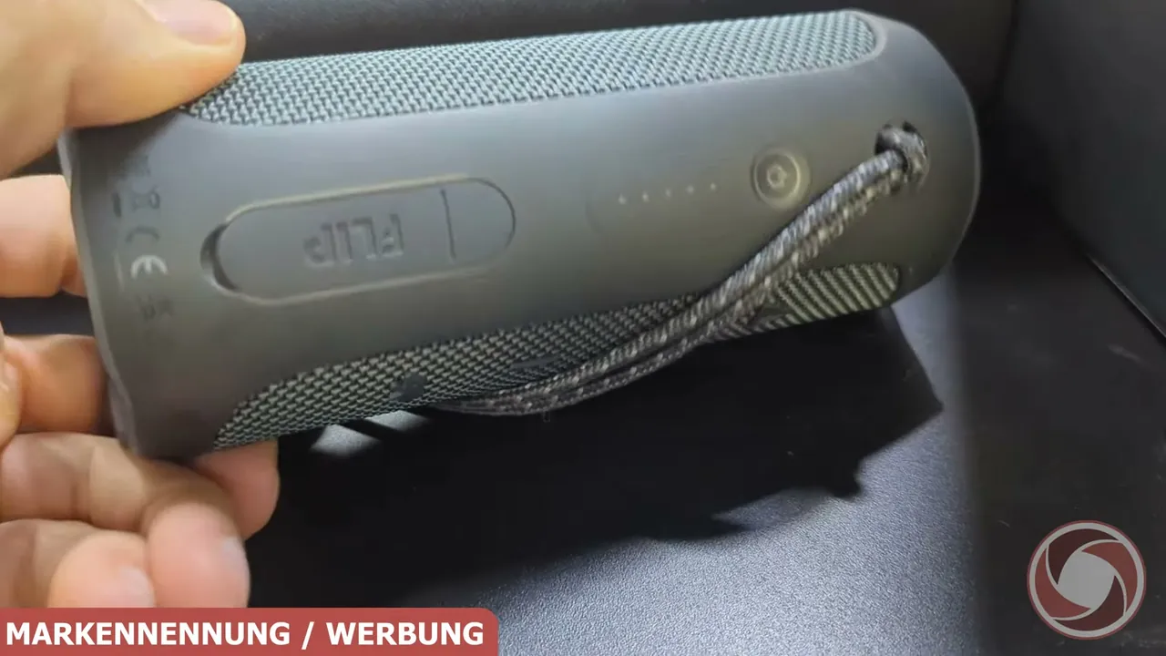 Auf der Rückseite befinden sich die Einschalttaste, eine LED-Akkustandsanzeige und eine robuste Trageschlaufe.