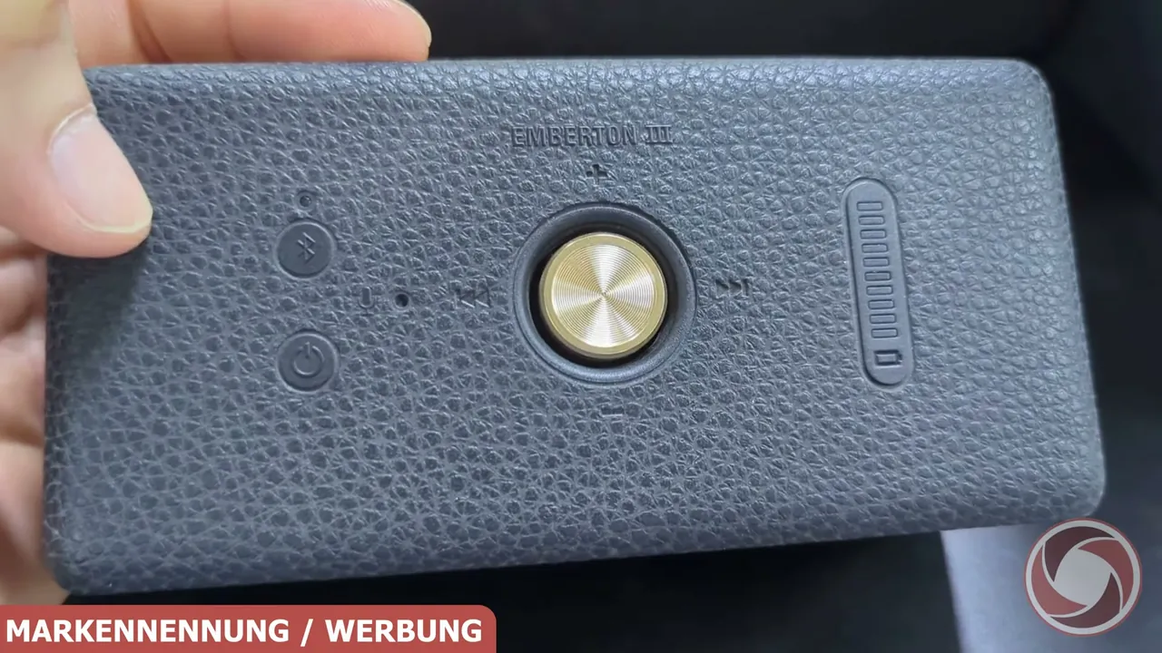 Auf der Oberseite sitzen der zentrale Steuerknopf in Messing-Optik, Funktionstasten und eine Balkenanzeige für den Akku.